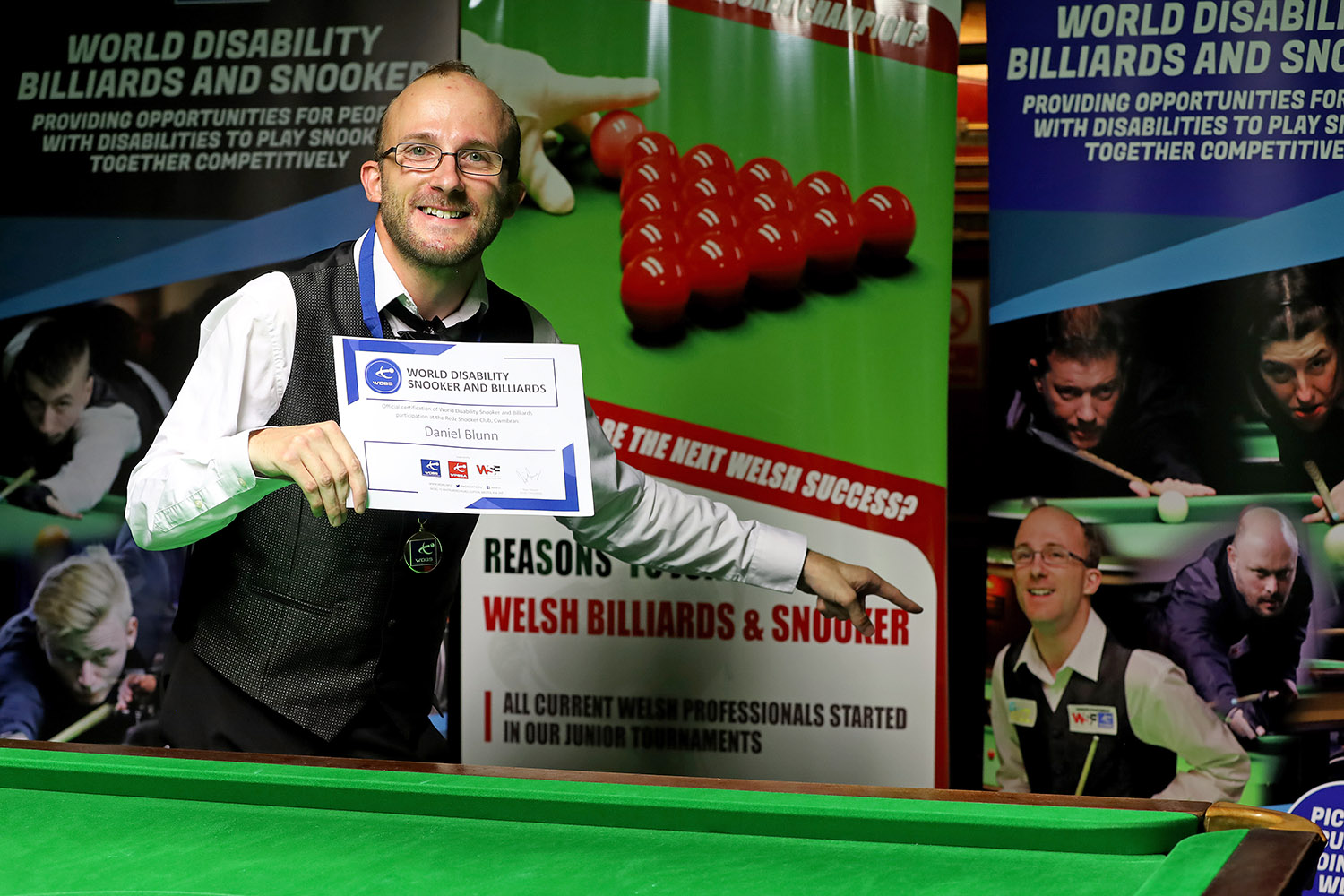 Daniel Blunn smiling and pointing to his own image on tournament banner