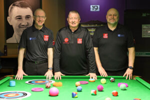 Coaches Andrew Highfield, Chris Lovell and Mark Peevers pose at the edge of the snooker table which is covered in various sensory snooker items including soft balls and targets