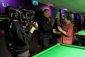 Coach Chris Lovell awards a medal to one of the participants of sensory snooker while the BBC cameras film the moment